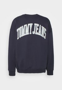 Navy blue sweatshirt with a crew neck, wide sleeves, and a curved "TOMMY JEANS" text design in light blue across the chest. Soft texture.