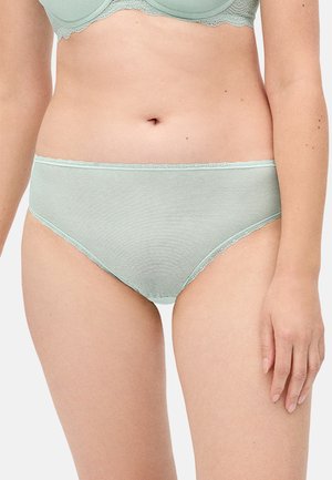 Mujer con bragas texturizadas verde claro y sujetador a juego, mostrando la zona media y los muslos superiores contra un fondo liso.