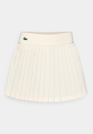 Gonna plissettata alla lunghezza del ginocchio in tessuto crema, con una cintura a coste e un piccolo logo verde. Texture liscia e design strutturato.