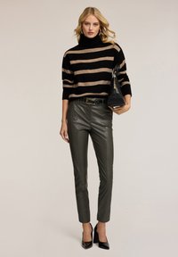 Sweter w paski w kolorze czarno-beżowym z golfem, oliwkowe spodnie z wysokim stanem, czarny pasek i czarna torebka; błyszczące czubate szpilki.