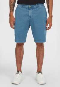 Lichtblauwe shorts van katoen met een relaxte pasvorm, voorzien van een knoopsluiting, zijzakken en opgerolde hems. Gedragen met witte sneakers.