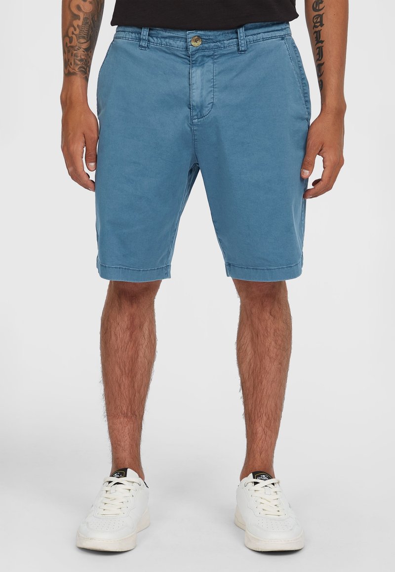 Lichtblauwe shorts van katoen met een relaxte pasvorm, voorzien van een knoopsluiting, zijzakken en opgerolde hems. Gedragen met witte sneakers.
