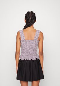 Levandulový květinový top s nařasenými ramínky, spárovaný s černou sukní, která má úzký pas a rozšířený lem.