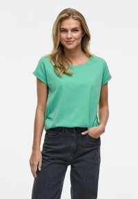 Mintgrön, kortärmad t-shirt med rund halsringning, i kombination med hoftaxerade svarta jeans. Slät textur och avslappnad passform.