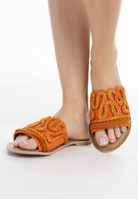 Narancssárga textil csúszó szandál, texturált kötél részletezéssel. Lapos talp, lekerekített nyitott orra és bonyolult varrás az élein.