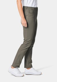 Olijfgroene broek met een slim fit, elastische tailleband en zijzakken, gecombineerd met witte sportschoenen. Soepele stoftextuur.