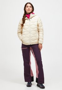 Puffy cremefarvet jakke med vandret quiltet mønster og hætte, kombineret med mørkelilla bukser med lyserøde sidepaneler og lynlåse.