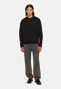 Sudadera negra de cuello redondo de algodón, con un logo minimalista. Combinada con jeans azul desgastado de corte relajado y zapatos negros.
