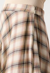 Rutet nederdel i beige med en blanding af brune, sorte og lyserøde striber. Lavet af blødt stof med lynlås i taljen.