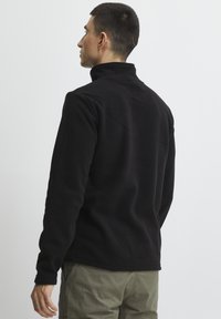 Sort fleece-pullover med høj krave og lange ærmer, der har en glat tekstur og minimale sømme. Bagfra ses et enkelt design uden dekorationer.