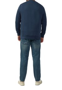 Sweatshirt bleu marine à col rond, avec des poignets et un ourlet côtelés. Porté avec un jean en denim bleu clair et des baskets beiges. Détails de couture visibles.