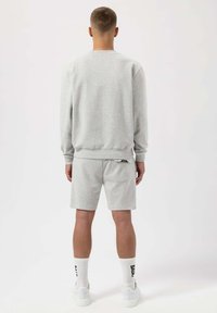 Felpa grigia con maniche lunghe, colletto a girocollo e polsini a coste, abbinata a pantaloni corti grigi coordinati. Sneakers bianche e calzini visibili.