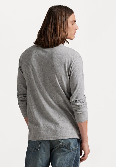 Γκρίζο μακρυμάνικο μπλουζάκι από μαλακό υλικό, με στρογγυλή λαιμόκοψη και ελαφρώς κυλιόμενα μανίκια. Συνδυάζεται με τζιν παντελόνι.