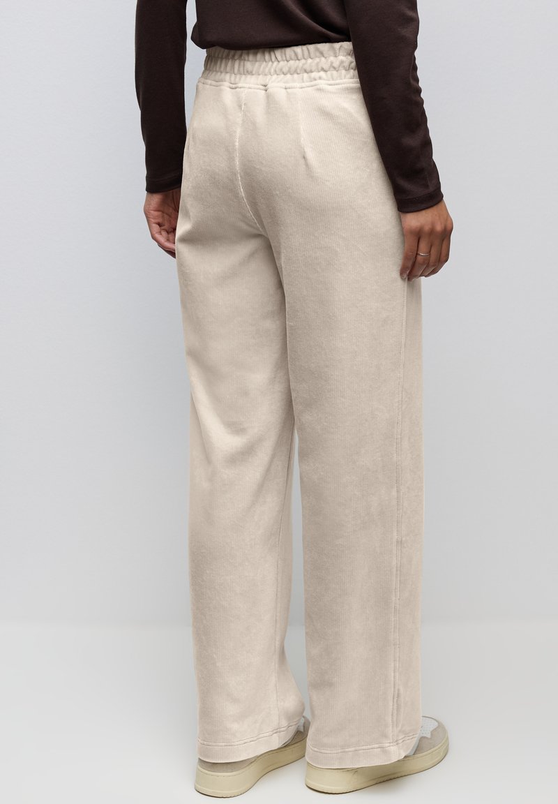 Pantalons larges beige en tissu doux et texturé avec une taille élastique, dotés de poches latérales et d'une coupe décontractée.