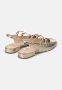 Metalen gouden slingback schoenen met een lage blokhak, open teen, uitsnijdingen aan de zijkanten en decoratieve kwastjes op de bandjes. Gladde, reflecterende textuur.