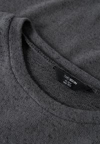 Harmaa neulepaita, jossa pyöreä pääntie, teksturoitu kangas ja etiketti, jossa lukee "TWO SOON" ja koko 11-12 vuotta. Sileä ja pehmeä ulkonäkö.