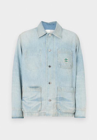 Ανοιχτό μπλε τζιν μπουφάν με κουμπωτή μπροστινή όψη, μυτερό γιακά, δύο μπροστινές τσέπες και ένα μικρό μπρελόκ με την επωνυμία στην τσέπη στο στήθος.