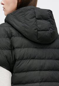 Fekete bélelt kabát kapucnival, steppelt mintával és sima textúrával. A szövet fényes felületű, finom varrásmintákkal.