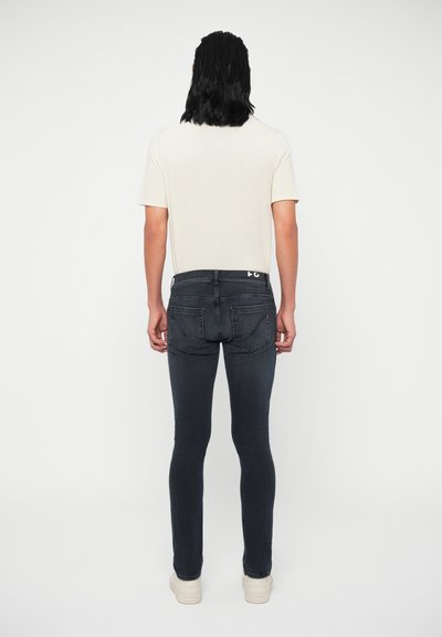 Σκούρα τζιν skinny με ψηλή μέση, διαθέσιμες πίσω τσέπες και διακριτές ραφές, συνδυασμένα με ένα ανοιχτό μπεζ μπλουζάκι.