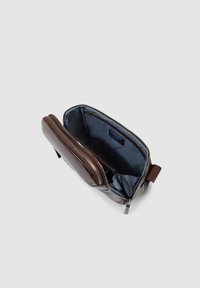 Borsa da toilette in pelle marrone aperta per mostrare l'interno in tessuto blu con tasca con cerniera e scomparto principale su uno sfondo neutro.