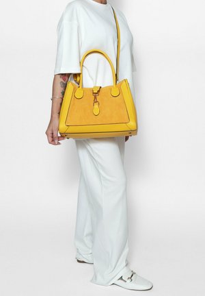 Geel suede handtas met een gestructureerd ontwerp, dubbele bovenhandvatten en een verstelbare schouderriem. Beschikt over een centrale sluiting en contrasterende stiksels.