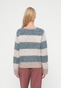 Rūtainā džemperis ar bēšiem, gaiši ziliem un tumši ziliem toņiem, ar ribotu apakšmalu un mīkstu, teksturētu dziju. Brīvā piegriezumā ar garām piedurknēm.