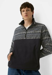 Fleece pullover med et mønstret grå og blå øverste sektion, solid mørkeblå nederste sektion, halv-zip krave og sidelomme.