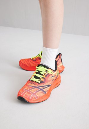 Chaussures de sport orange vif avec des accents noirs et des lacets vert fluo. Présentent un motif texturé et des semelles rembourrées pour un soutien optimal.