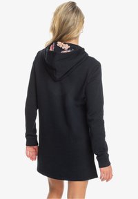Robe à capuche noire avec une doublure à motif floral dans la capuche, manches longues et texture douce. Présente une coupe décontractée et un design à mi-genou.