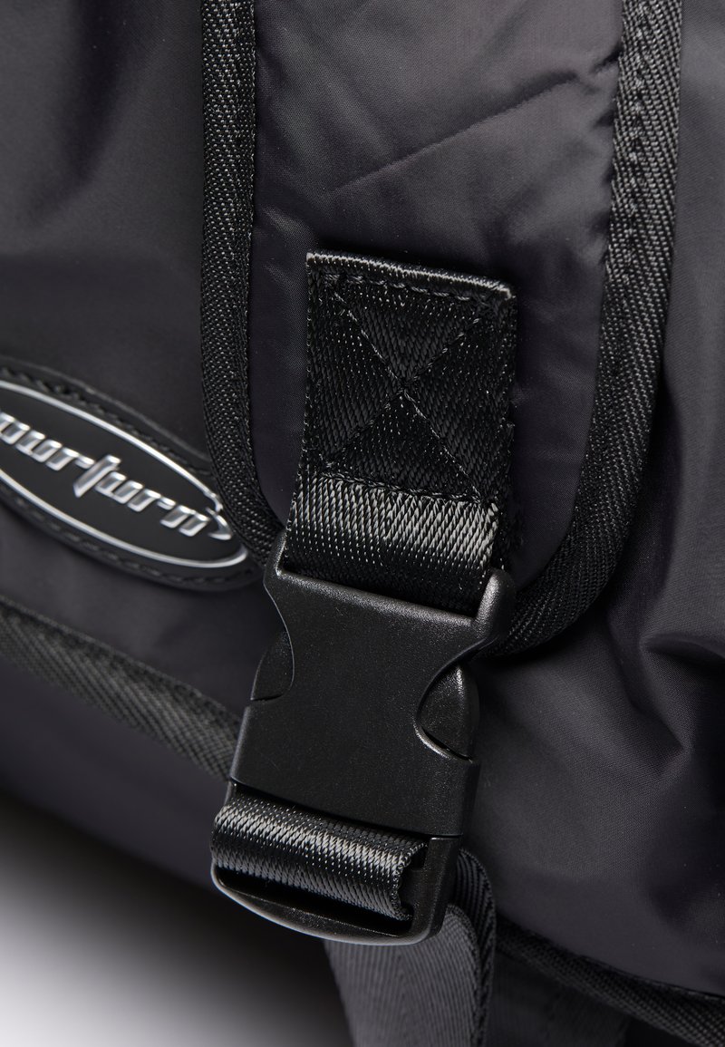 Correa de nailon negra con hebilla de plástico, con superficie texturizada y detalles de costura, unida a una bolsa con un logo.