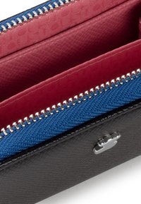 Portafoglio nero con interni in tessuto rosso e blu, dotato di una cerniera e accessori in metallo argentato. Superfici testurizzate e distinti scomparti colorati sono visibili.