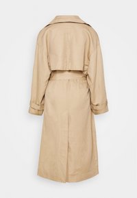 Trench-coat long beige vu de dos avec col large, manches longues avec sangles, taille ceinturée et patte d'ouragan au dos.