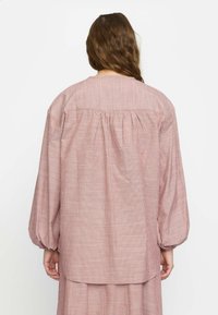 Röd och vit randig blus med långa puffärmar. Har en rynkad bakdesign och rund halsringning, tillverkad av lätt material.