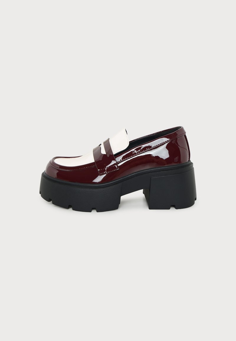Χοντρό loafer με πλατφόρμα σε βυσσινί λουστρίνι, λευκές λεπτομέρειες και χοντρή μαύρη καουτσούκ σόλα σε ανοιχτό γκρι φόντο.