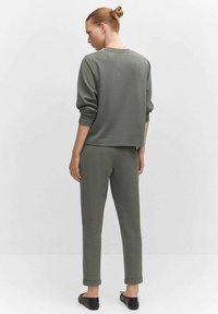 Olijfgroen sweatshirt en bijpassende joggers, beide van zacht materiaal. Het sweatshirt heeft een relaxte pasvorm; de joggers zijn taps toelopend met een boord aan de onderkant.