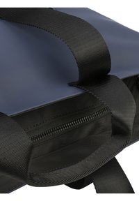 Sac bleu marine en matériau synthétique lisse avec des poignées en tissu noir et une poche zippée à l'intérieur. Forme plate avec un design robuste.
