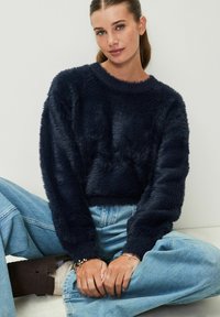 Maglione corto blu navy con una texture morbida e pelosa, dotato di scollatura tonda e maniche lunghe, abbinato a jeans a gamba larga blu chiaro.