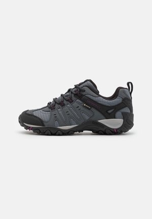 Chaussure de randonnée basse gris foncé et noire avec semelle robuste, devant à lacets et étiquette imperméable GORE-TEX sur le côté.
