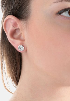 Close-up af en kvindes øre med en rund sølvnitteørering med en tekstureret overflade.