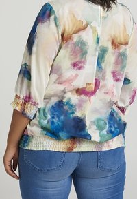 Blouse multicolore avec des motifs abstraits en aquarelle dans des tons pastel. Elle présente un ourlet froncé et des manches trois-quarts, confectionnée en tissu léger.