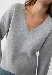 Grauer gerippter Strickpullover mit weitem V-Ausschnitt und abgesenkten Schultern, der einen lockeren Sitz und eine strukturierte Stoffoberfläche bietet. Einfaches und vielseitiges Design.