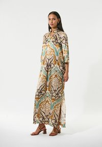Robe longue et fluide en tissu transparent, avec un motif floral dans des teintes de marron, turquoise et crème. Elle possède un col mandarin et des fentes latérales.