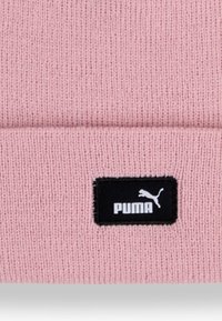 Világos rózsaszín kötött sapka, hajtott peremmel; fekete téglalap alakú folt található rajta fehér "PUMA" felirattal és logóval.