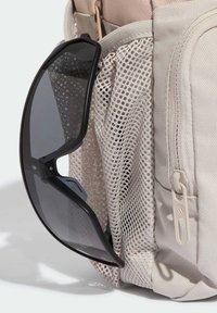Borsa beige con tessuto testurizzato e tasca in rete che contiene occhiali da sole neri. Presenta una zip color crema e accessori a clip.