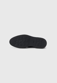 Suela de zapato de goma negra con patrón texturizado y ranuras para tracción. Acabado suave con el logotipo de la marca grabado en el lado.