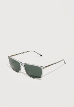 Gafas de sol rectangulares transparentes con lentes verde oscuro y brazos de metal plateado, con acentos dorados en las bisagras.