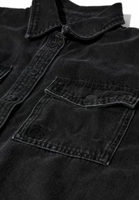 Schwarzes Jeanshemd mit einem Button-Down-Kragen, zwei Brusttaschen, dezenten Steppdetails und einem Logopatch auf der linken Tasche.