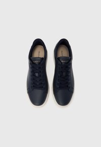 Granatowe skórzane sneakersy o gładkiej fakturze, zaokrąglonym nosku, kontrastującej białej gumowej podeszwie oraz czarnych sznurowadłach. Logo na języku w kolorze złotym.