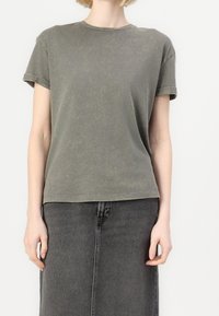 Oliwkowa bawełniana koszulka z okrągłym dekoltem, krótkimi rękawami i luźnym krojem. Materiał ma miękką, lekko postarzającą fakturę.