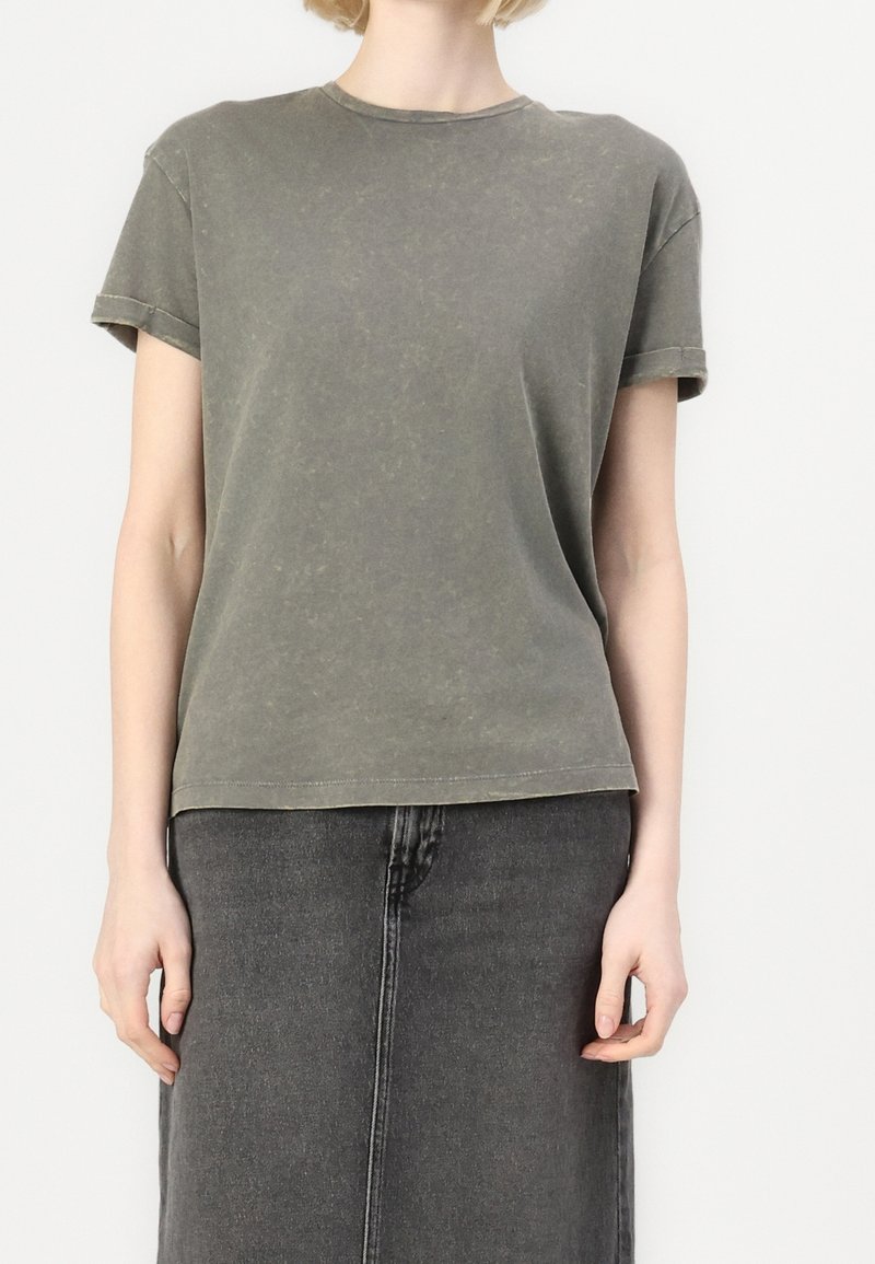 Oliwkowa bawełniana koszulka z okrągłym dekoltem, krótkimi rękawami i luźnym krojem. Materiał ma miękką, lekko postarzającą fakturę.